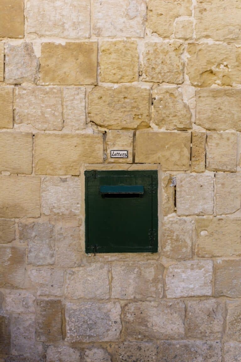 A green mailbox set into a stone wall.